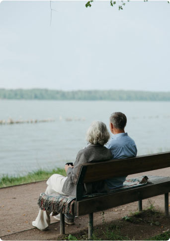 An older couple sitting on a lakeside bench